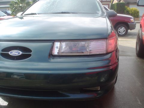1993 Ford Taurus - The front of a green Ford Taurus is visible, parked next to other vehicles.