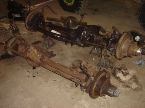 1992 Ford Bronco - Two vehicle axles, one rusty and one black, are displayed on a concrete floor.