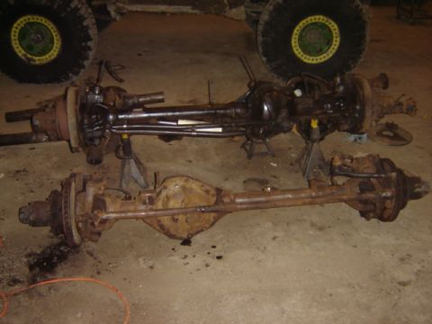 1992 Ford Bronco - Two vehicle axles are displayed on a concrete floor, one appearing to be a newer replacement and the other showing significant rust.