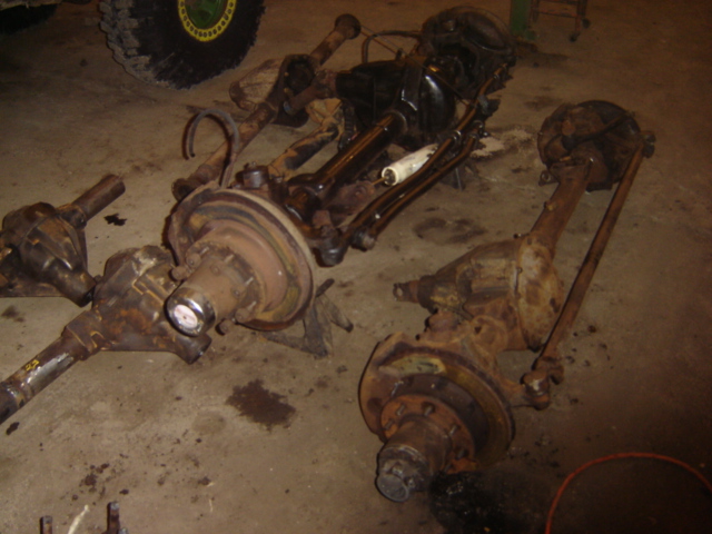 Several vehicle axles and differential assemblies are laid out on a concrete floor