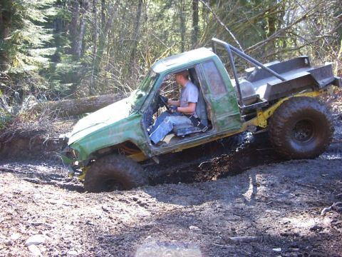 1990 Ford Bronco - A modified off-road vehicle navigates a muddy trail in a wooded area.