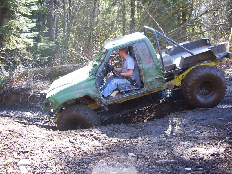 Green off-road vehicle stuck in mud, driver visible inside