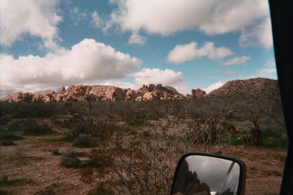 Desert landscape with rock outcrops under a cloudy sky, seen past a vehicle side mirror