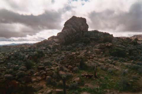 1990 Ford Bronco - boulder-strewn desert hillside rises to a jagged rock crag at its summit beneath a heavily clouded sky.