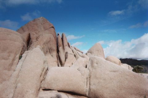 1990 Ford Bronco - formation of smooth tan granite boulders stacked into jagged angular peaks stands against a bright blue cloudy sky.