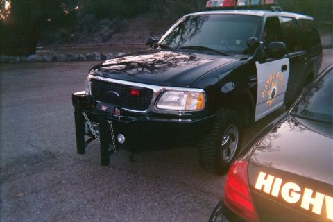 1990 Ford Bronco - black-and-white Highway Patrol SUV fitted with a front brush guard and light bar parked next to a marked patrol sedan at dusk.