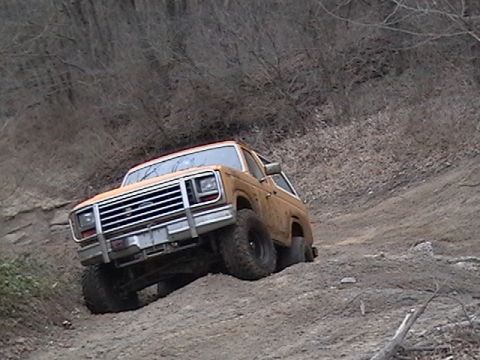 1986 Ford Bronco - An orange SUV navigates a steep dirt incline, its front grille and bumper clearly visible.