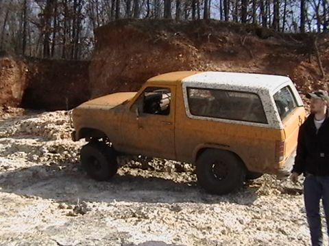 1986 Ford Bronco - This muddy Ford Bronco navigates a challenging off-road terrain with a dirt embankment in the background.