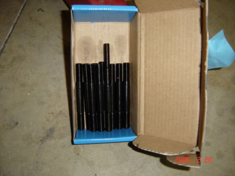 1990 Ford Bronco - An open cardboard box on a concrete floor holding a set of black oxide threaded main studs standing upright in a blue insert. The empty hal…