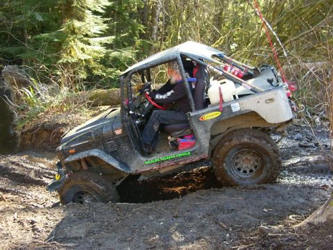 1990 Ford Bronco - An off-road vehicle navigates a muddy trail through a forest.