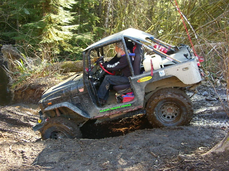 Black off-road vehicle with roll cage stuck in mud, driver visible