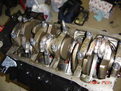 1990 Ford Bronco - Bottom view of an inverted black-painted V8 engine block with the crankshaft, main caps and connecting rods installed, secured by studs wit…