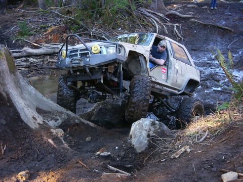 1990 Ford Bronco - This heavily modified off-road vehicle is shown attempting to climb over large rocks on a challenging trail.