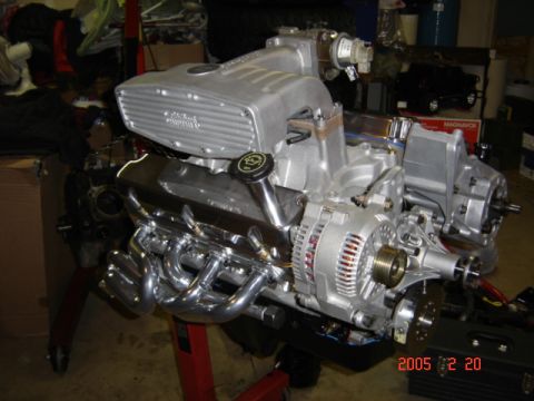 1990 Ford Bronco - Assembled fuel-injected V8 on a red engine stand in a garage, wearing a polished aluminum upper intake plenum, black valve cover with a chr…