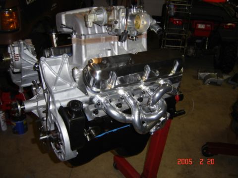 1990 Ford Bronco - Rear three-quarter view of an assembled fuel-injected V8 mounted on a red engine stand, showing the cast aluminum intake with throttle body…