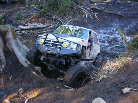 1990 Ford Bronco - Off-road vehicle with custom bumper and large tires navigating a challenging muddy trail.