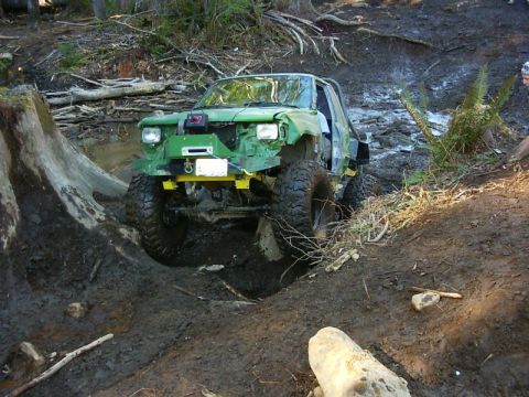 1990 Ford Bronco - This heavily modified off-road vehicle appears to be stuck in a muddy terrain, with its front end damaged.
