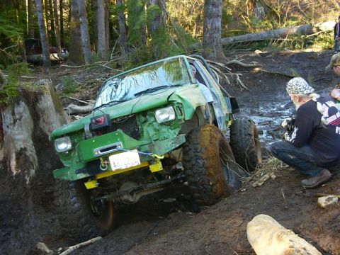 1990 Ford Bronco - This heavily modified off-road vehicle is stuck in a muddy forest terrain, showing signs of extensive use.