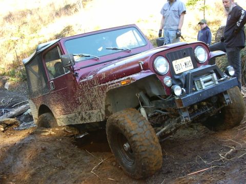 1990 Ford Bronco - A maroon Jeep CJ-7 is stuck in the mud off-road, with several people observing the situation.