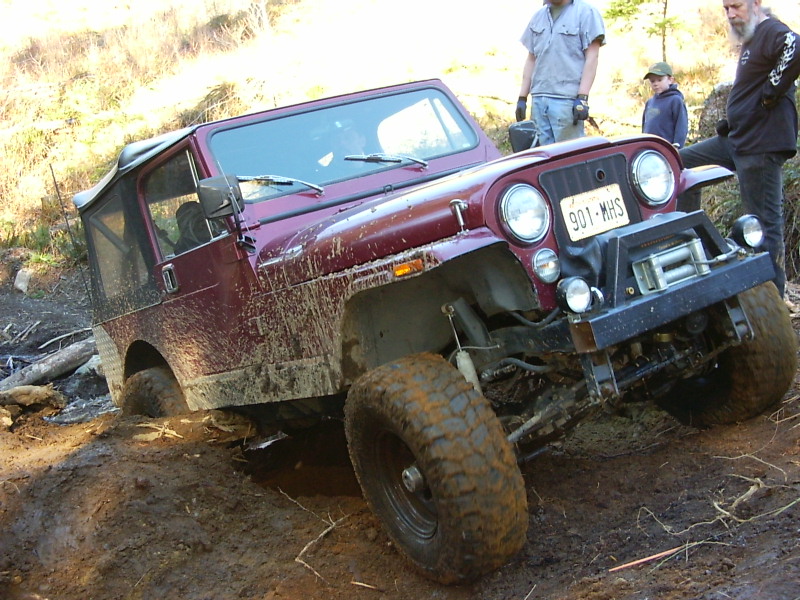 Maroon Jeep CJ-7 stuck in mud, winch on front bumper, people watching