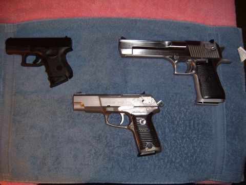 1993 Ford Bronco - Three semi-automatic pistols arranged on a blue towel: a black subcompact polymer pistol, a stainless Desert Eagle, and a stainless Ruger P…