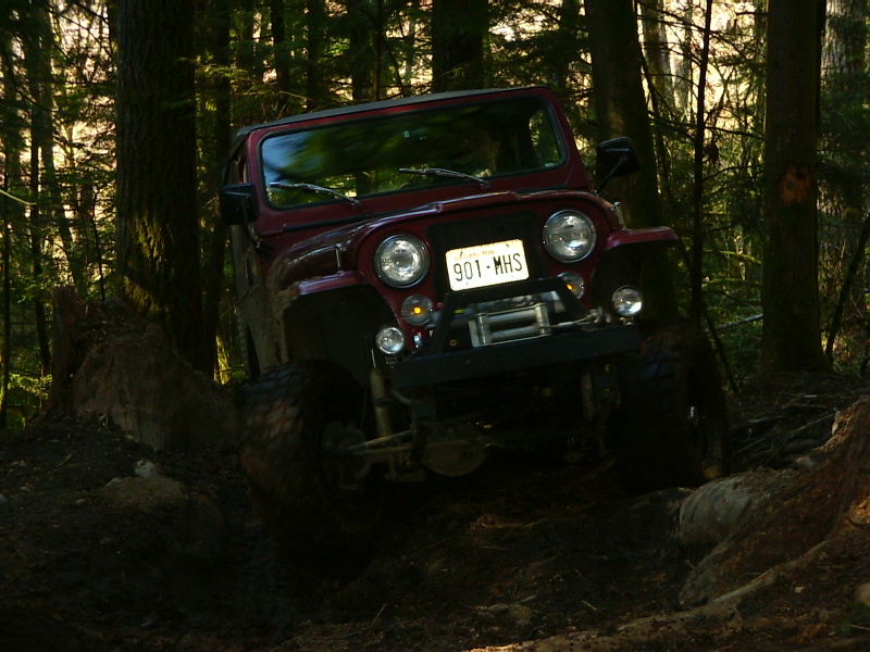 Red Jeep CJ-7 off-roading on a muddy trail with trees