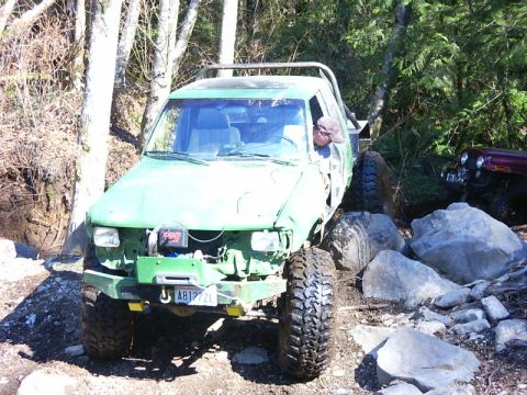 1990 Ford Bronco - This modified green off-road vehicle is seen navigating a challenging rocky trail with another vehicle visible in the background.