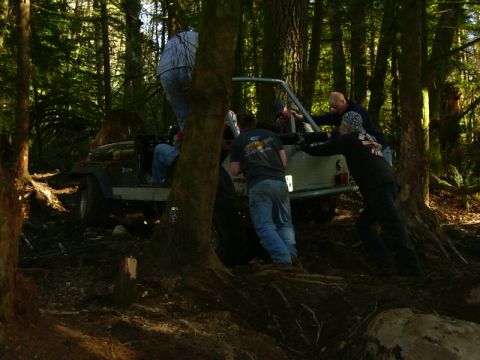 1990 Ford Bronco - A group of people are pushing a Jeep Wrangler through a wooded area.