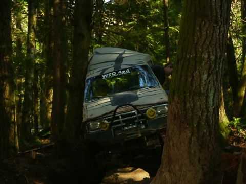 1990 Ford Bronco - Off-road vehicle navigating a difficult trail through a dense forest.