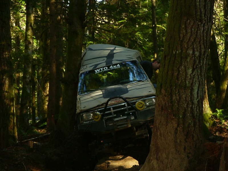 Off-road vehicle with "WTO 4X4" sticker on windshield is stuck between trees on a trail