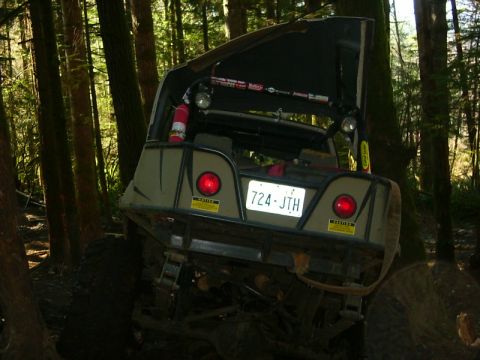 1990 Ford Bronco - An off-road vehicle is stuck in the mud on a wooded trail, its rear end angled upwards.