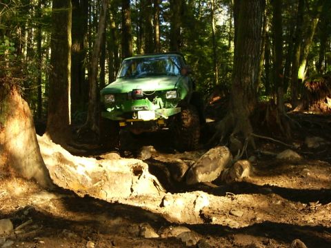 1990 Ford Bronco - A green off-road vehicle tackles a challenging rocky path through a dense forest.