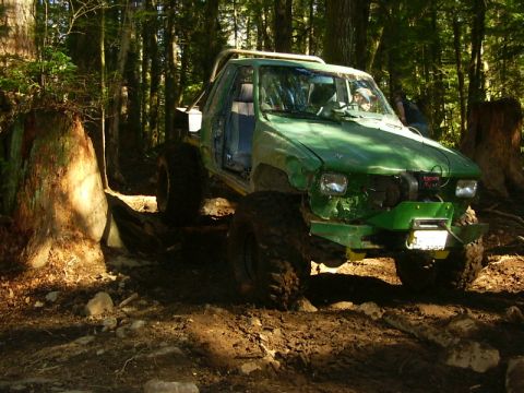 1990 Ford Bronco - Off-road truck with significant modifications driving through a wooded area.