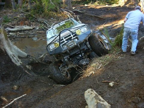 1990 Ford Bronco - Off-road vehicle navigating a difficult muddy terrain, with a person observing.
