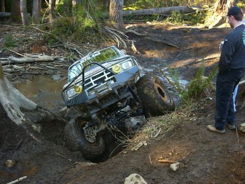1990 Ford Bronco - This heavily modified off-road vehicle is navigating a challenging muddy terrain with a person observing the action.
