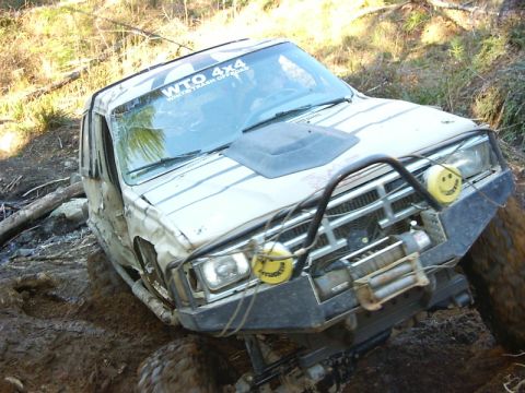 1990 Ford Bronco - An off-road vehicle navigates a muddy terrain, equipped with a winch and auxiliary lights.
