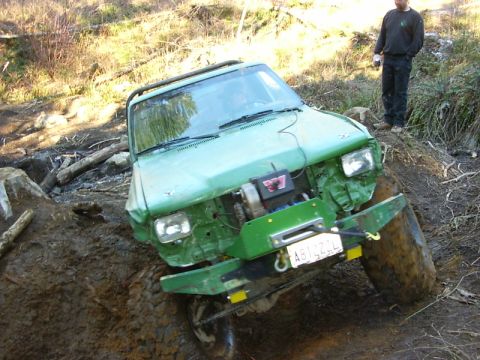 1990 Ford Bronco - This green off-road vehicle appears to be stuck in a muddy, wooded area, with a winch mounted on the front.