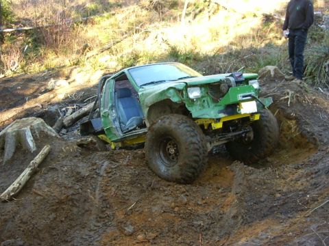 1990 Ford Bronco - Modified off-road vehicle with large tires stuck in mud, front end damaged.