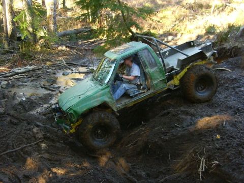 1990 Ford Bronco - A modified green truck navigates a challenging muddy terrain, with its tires deep in the mire.