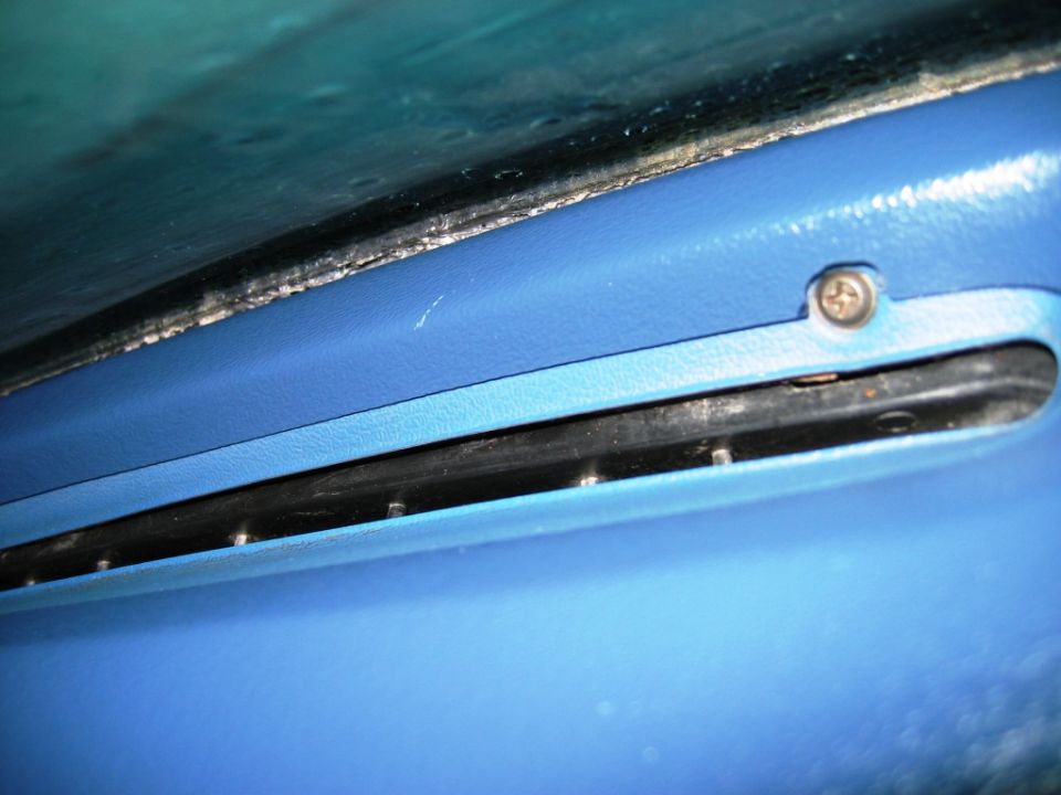 Blue vehicle interior trim panel with a Phillips screw and black seam channel