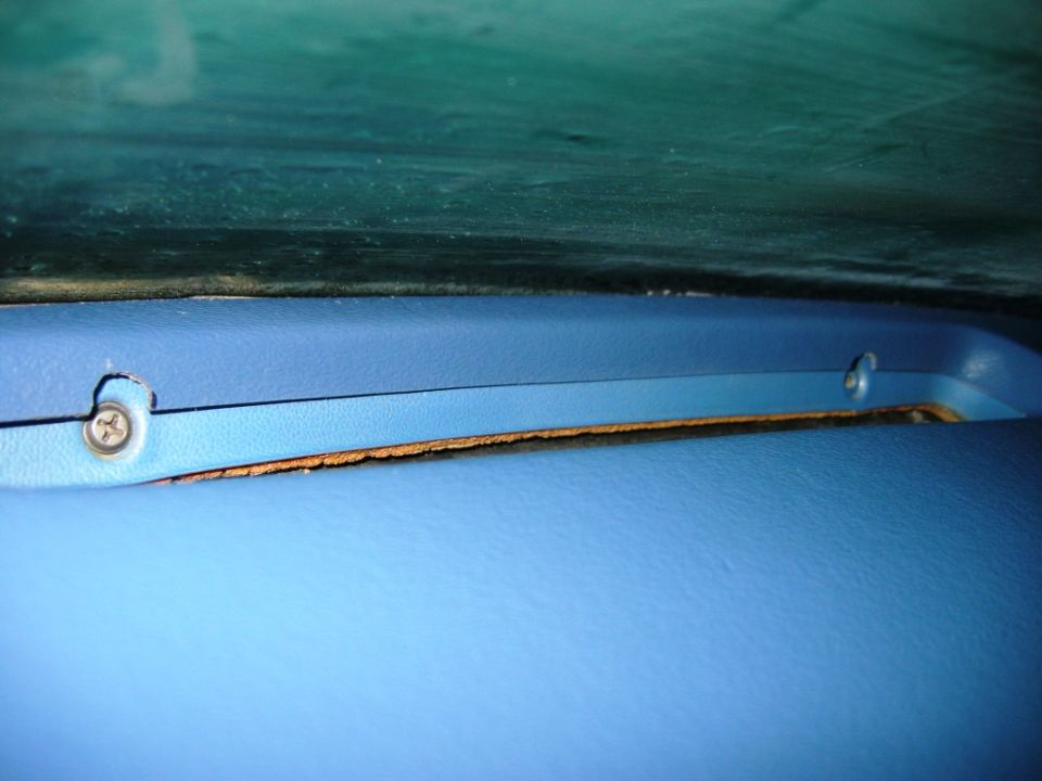 Blue interior trim panel with screw and gap exposing worn board below a windshield edge