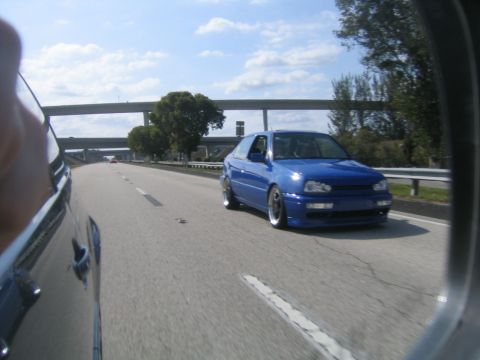 1998 Volkswagen Jetta - A blue hatchback is captured driving on a highway under a cloudy sky.