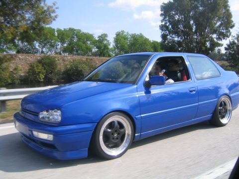 1998 Volkswagen Jetta - A blue coupe is captured in motion on a sunny day.