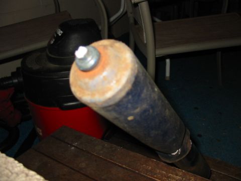 1985 Ford LTD Crown Victoria - A rusty metal cylinder is the focus, obscuring a shop vac and wooden planks.