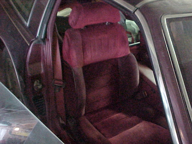 Burgundy cloth driver's seat and door panel seen through open door of maroon car in a garage