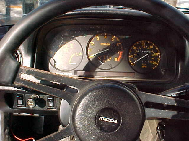 Instrument cluster and Mazda steering wheel showing tachometer, speedometer, and odometer around 153,000 miles