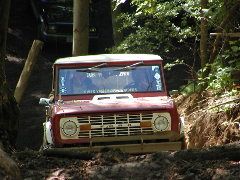 1975 Ford Bronco navigating a muddy trail, another vehicle visible behind it
