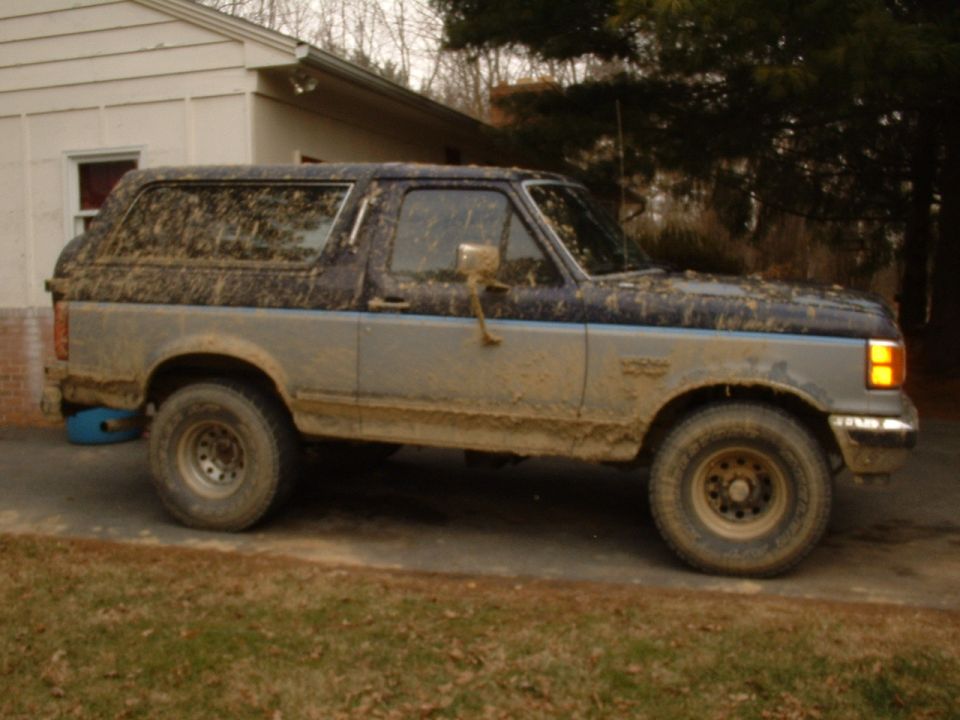 Mud-covered blue and silver full-size Ford Bronco side view on a driveway