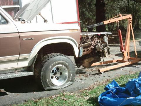 1982 Ford Bronco - The engine has been removed from this Ford Bronco and is being supported by an engine hoist. The front passenger tire is flat.