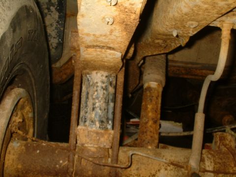 1982 Ford Bronco - Close-up view of the heavily rusted undercarriage of a vehicle, revealing suspension parts and a tire.